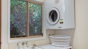 A laundry area with a front-loading washing machine, a white sink, and a window with a view of trees.