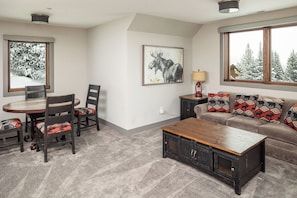 Un salon comprenant un canapé, une table basse, une table à manger avec des chaises, une lampe et un tableau accroché au mur.