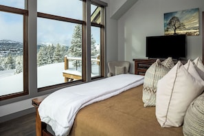 Une chambre à coucher avec un lit, une télévision et une grande fenêtre donnant sur un paysage enneigé.
