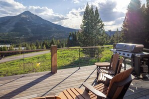 Una terraza con una parrilla, sillas y vistas a una montaña.