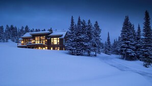 Schneebedeckte Landschaft mit einer zweistöckigen Lodge, die einen Balkon und große Fenster hat.