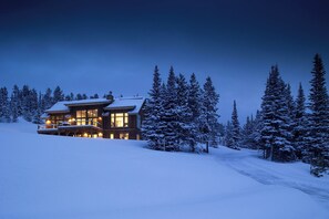 Paisaje nevado con un albergue de dos pisos, con balcón y ventanas grandes.