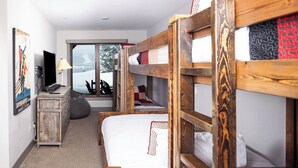 Ein Zimmer mit Etagenbetten, einem Schreibtisch, einem Stuhl, einer Lampe und einem Fenster mit Blick auf schneebedeckte Bäume.