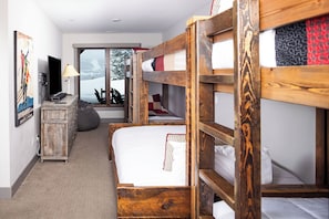Una habitación con literas, un escritorio, una silla, una lámpara y una ventana con vista a árboles nevados.