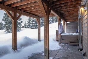 Une cabane en bois avec un porche couvert, un jacuzzi et un paysage enneigé en arrière-plan.