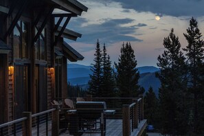Une terrasse en bois, avec des chaises et une table, d’où l’on peut admirer un paysage montagneux parsemé d’arbres.