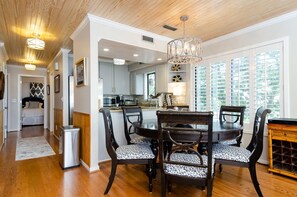 Un coin repas avec une table et des chaises en bois, un lustre, et une vue sur la cuisine et le salon.