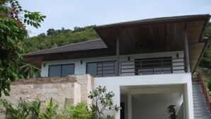 A modern two-story house with a covered driveway, stone wall, and a motorcycle parked inside. - 2 Bedroom Pool Villa Nature SDV004 By Samui Dream Villas (Mae Nam)