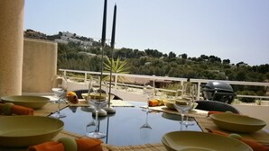 Une table à manger dressée avec des bols, des verres à vin et des serviettes, offrant une vue panoramique sur une colline pittoresque.