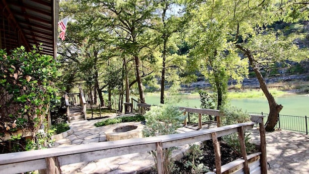 A stone pathway leading to a wooden deck with a fire pit, surrounded by trees and overlooking a body of water.