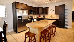 A modern kitchen with dark cabinets, stainless steel appliances, a central island with stools, and a clock on the wall.