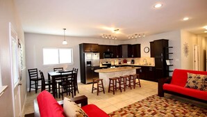 A modern kitchen with dark cabinets, a central island with stools, and a dining area with a red sofa and chairs.