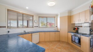 Een moderne keuken met een blauw aanrechtblad, houten kastjes, een inbouwoven en een raam met zonwering.