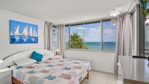 Ein Schlafzimmer mit einem Bett, einem Segelbootgemälde, einem Fenster mit Meerblick und einer Pflanze.