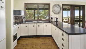 A kitchen with white cabinets, a black countertop, a large window, and a wall clock. - Pet friendly property with water views (Point Lookout)