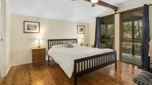 A bedroom with a wooden floor, a bed with a headboard, two bedside tables with lamps, and a view of a balcony through large windows. - Pet friendly property with water views (Point Lookout)