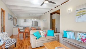 Una sala de estar moderna con un sofá, sillones y una mesa de centro. Se ve una cocina al fondo, con un comedor.