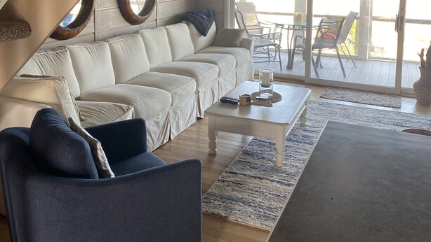 A modern living room with a white sofa, blue armchair, and a coffee table. A staircase with a wooden finish and a large window with a view of the outdoors. - Oceanfront Townhome With Breathtaking Views From 3 Deck Levels (Bethany Beach)