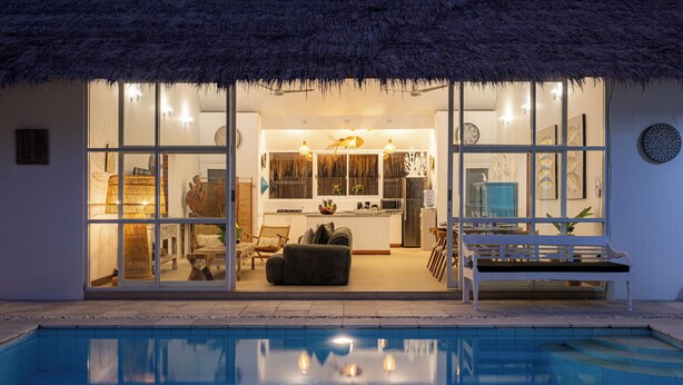 Una casa moderna con piscina, con zona pranzo, cucina e soggiorno dotati di tetto in paglia.