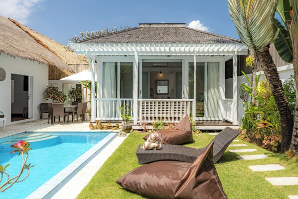 A poolside area with a covered seating area, a thatched-roof structure, and lush greenery.