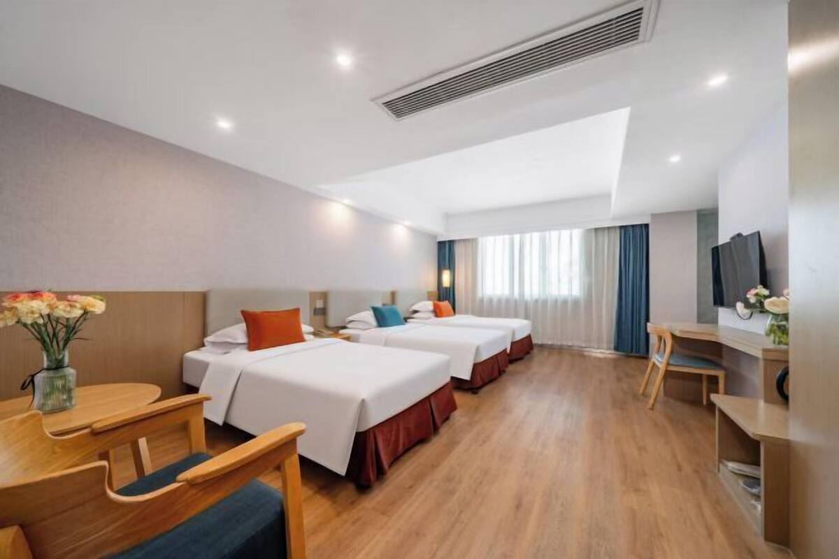 A hotel room with three beds, a desk, a chair, and a TV.