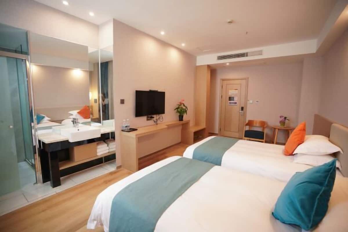 A hotel room with two beds, a desk with a computer, a TV, and a bathroom with a mirror and sink.