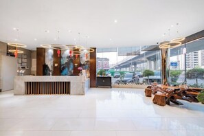 A modern reception area with a marble counter, wooden accents, and a view of the cityscape through large windows. - yiduo hotel (Hangzhou)