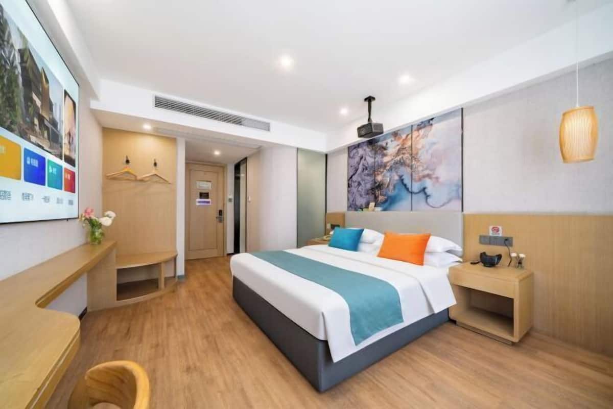 A hotel room with a bed, bedside table, nightstand, and a wall-mounted artwork.
