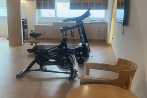 Egy szoba, melynek padlója fából készült, van benne egy étkezőasztal székekkel, és két állókerékpár.