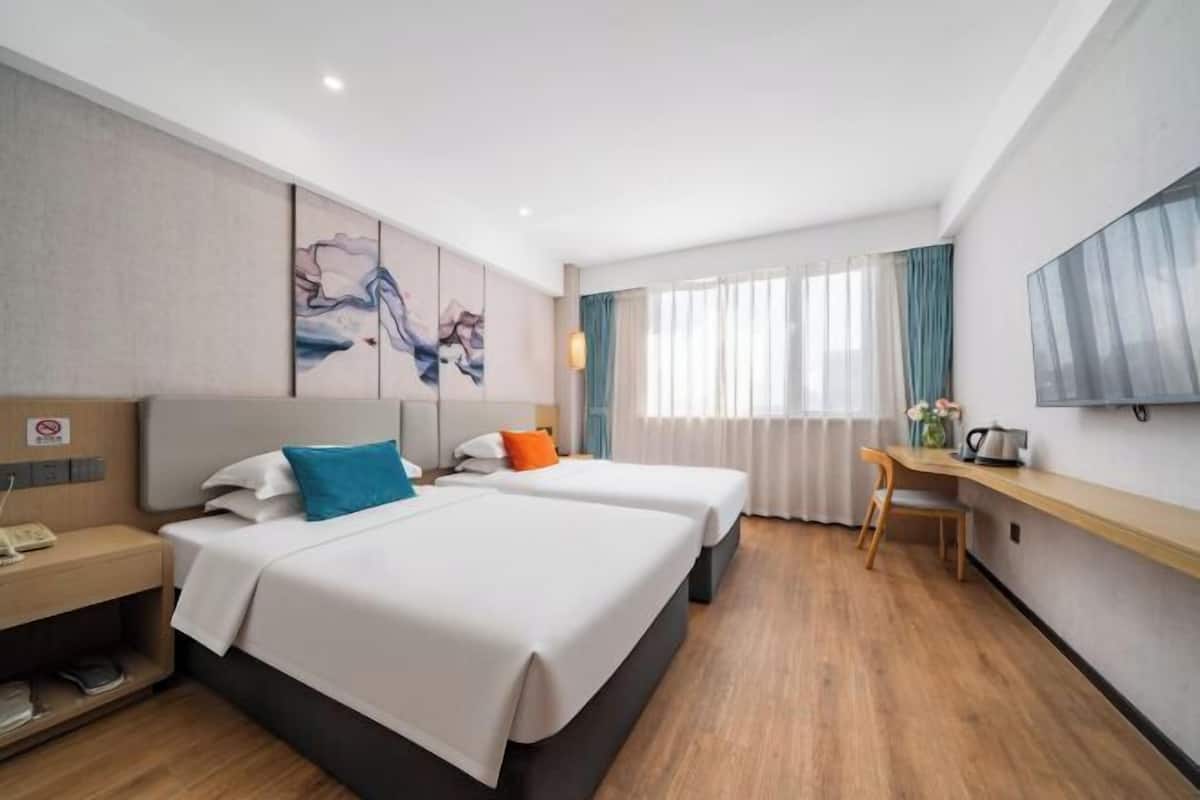 A hotel room with two beds, a desk, a chair, a TV, and artwork on the wall.