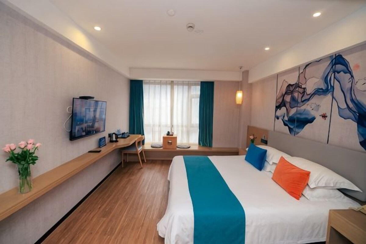 A hotel room with a bed, a desk, a TV, and a window with curtains.