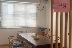 A room with a wooden dining table, chairs, a window with blinds, and a hanging light fixture. - yiduo hotel (Hangzhou)