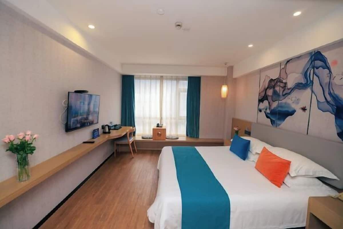 A hotel room with a bed, a desk, a chair, a TV, and a painting on the wall.