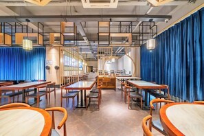 A restaurant interior with multiple dining tables and chairs, a kitchen area in the background, and blue curtains. - yiduo hotel (Hangzhou)