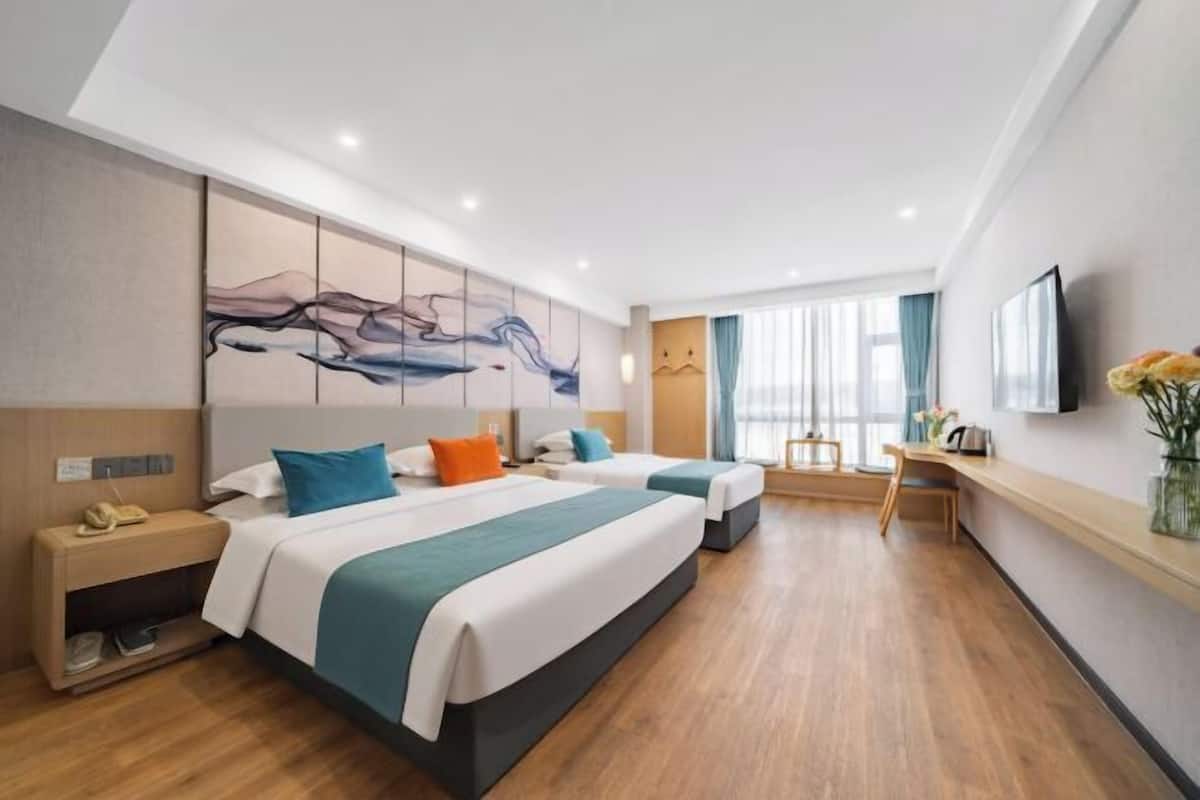 A hotel room with two beds, a desk, a chair, a TV, and a large abstract painting on the wall.