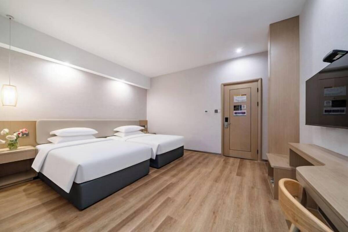 A hotel room with two beds, a desk, a chair, a TV, and a door.