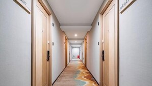 A hotel hallway with a carpeted floor, wooden doors, and a light-colored wall. - yiduo hotel (Hangzhou)