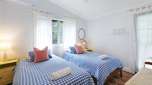Un dormitorio con dos camas, una mesita de noche con lámpara, un espejo y una ventana con cortinas.