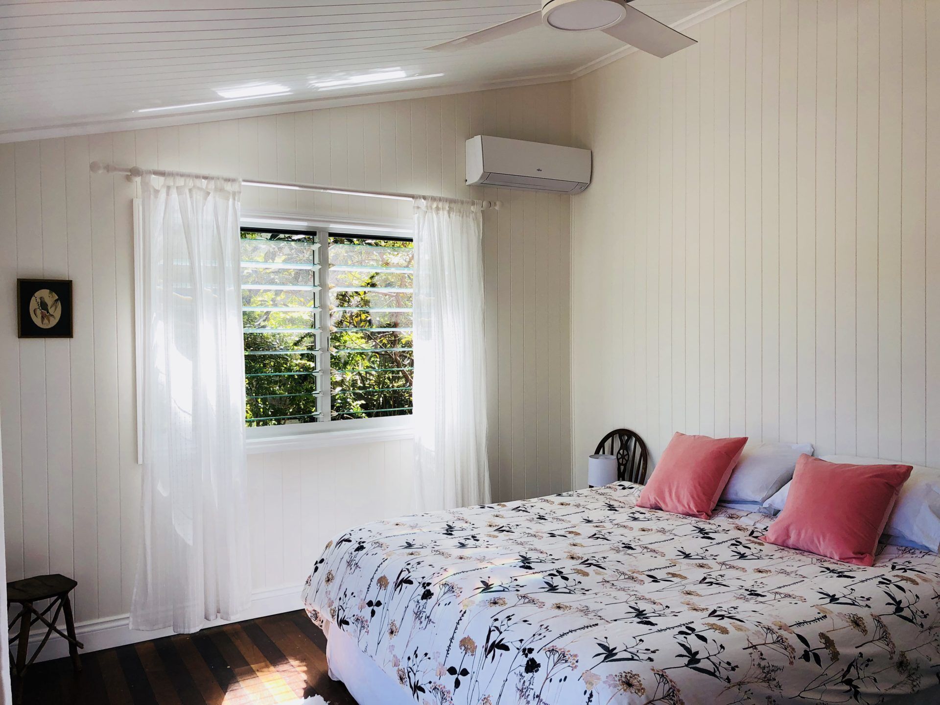Une chambre à coucher avec un lit, une fenêtre avec des rideaux, une chaise et un appareil de climatisation.
