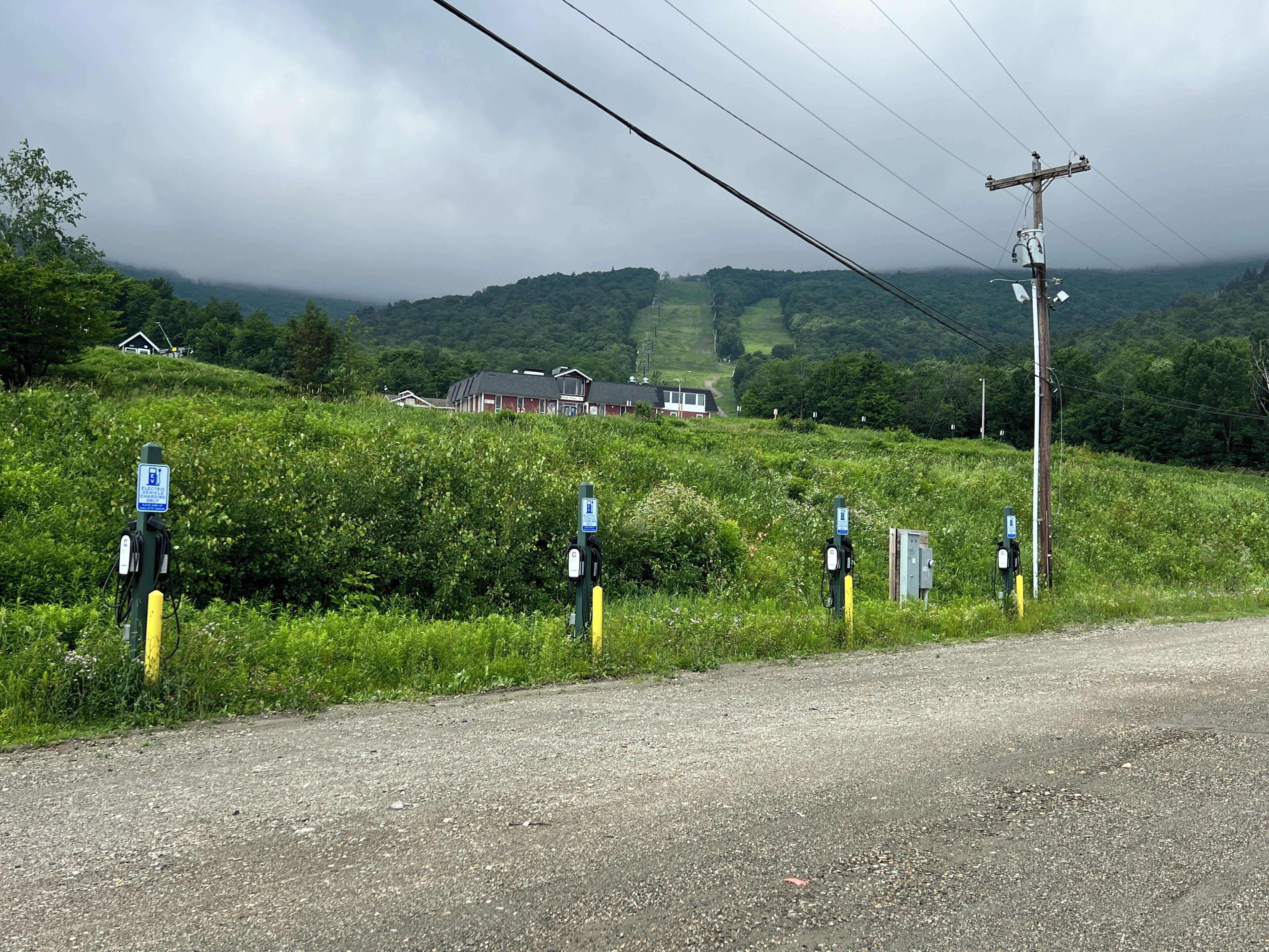 Une route de campagne avec des bornes de recharge pour véhicules électriques et une maison en arrière-plan.