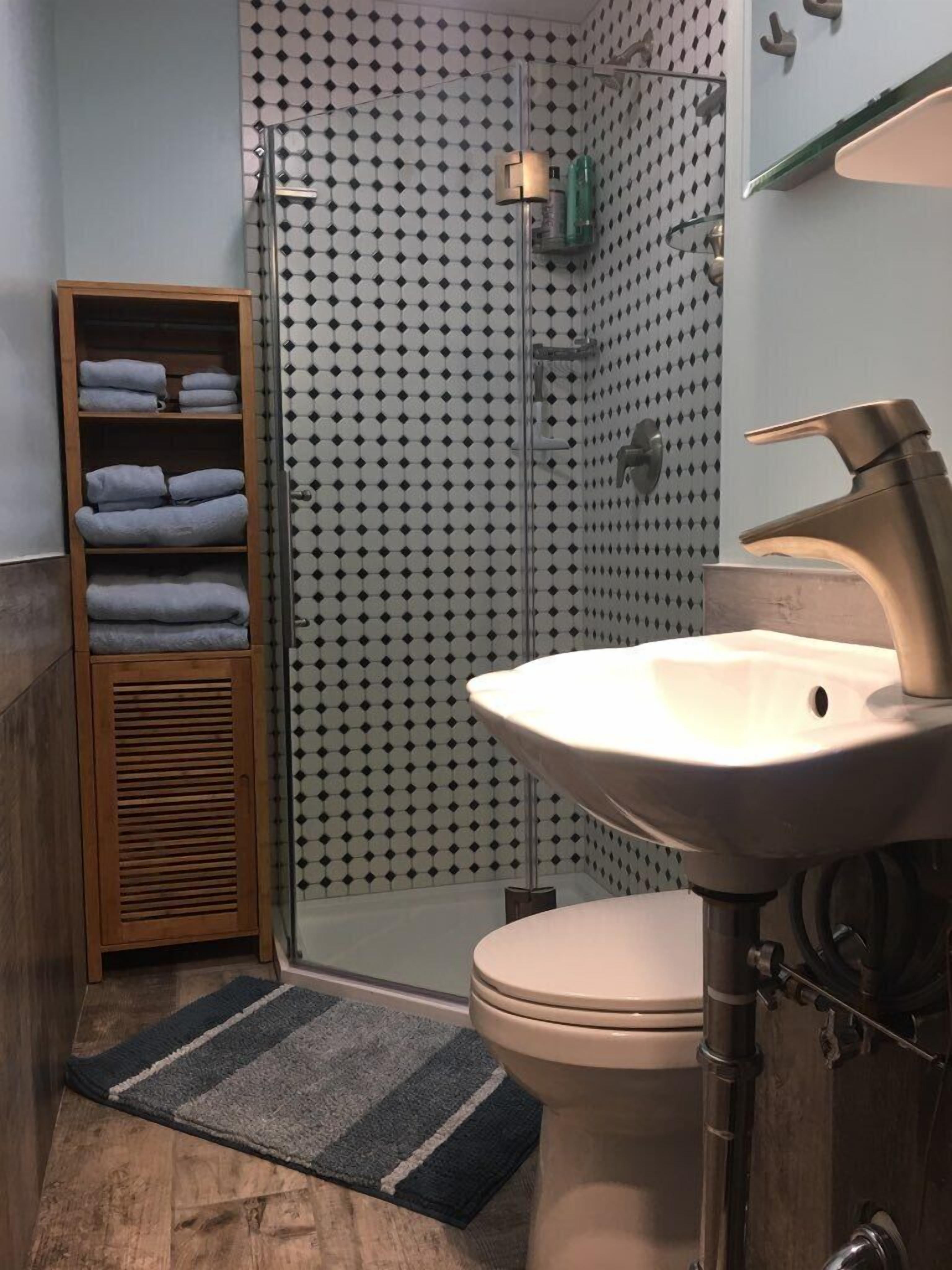 Un baño moderno con cabina de ducha de vidrio, un perchero de madera, un lavamanos con grifo moderno y un inodoro.