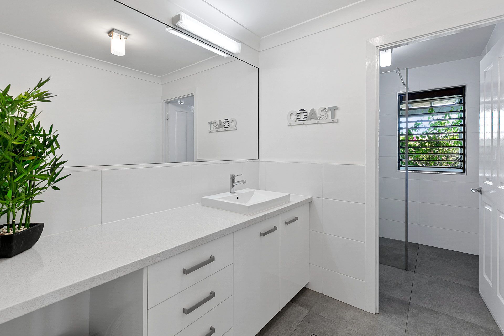 A modern bathroom with a white vanity, a large mirror, and a shower area.