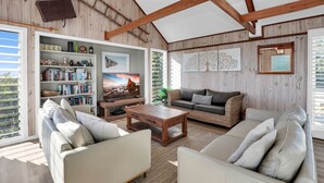 Ein geräumiges Wohnzimmer mit Holzbalkendecke, Bücherregal, Fernseher und einer Couch.