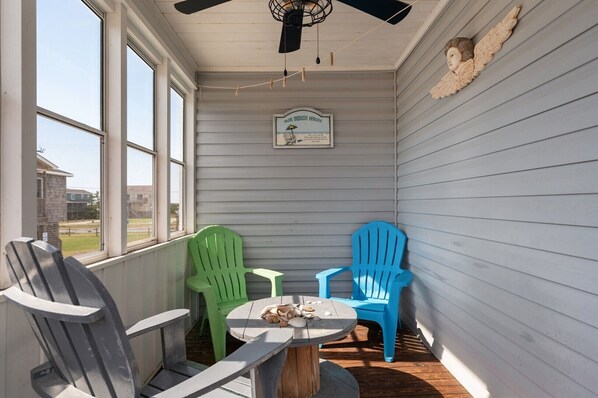 A covered porch with two Adirondack chairs, a small table, and a ceiling fan.