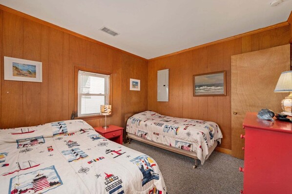 A room with two beds, wooden walls, a window, a door, and a red dresser.