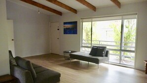 Ein geräumiges Wohnzimmer mit einer Couch, einem Couchtisch und einem großen Fenster mit Blick auf Grünflächen.