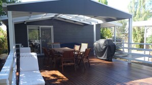 Eine überdachte Terrasse im Freien mit Holzdeck, einem Tisch mit Stühlen, einem Grill und einer überdachten Sitzecke.