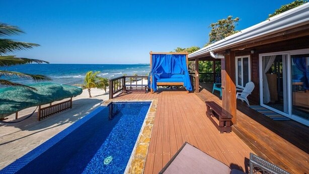 Una terraza de madera con piscina, un espacio de estar techado y vistas al océano.