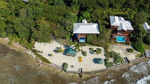 Una propiedad frente a la playa con dos edificios principales, una piscina y una zona arenosa con palmeras.