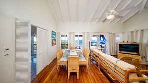 Un amplio salón con piso de madera, una mesa de comedor con sillas, un sofá, un televisor y un ventilador de techo.